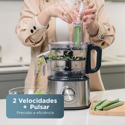 Person using a BLACK+DECKER food processor to slice green vegetables in a kitchen, bowl collecting slices.
