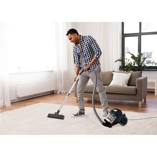 BLACKDECKER A7 vacuum cleaner in use on living room carpet with modern sofa and houseplants in background.