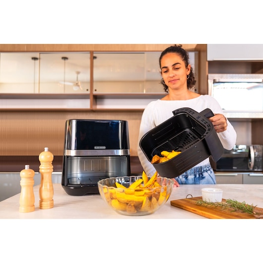 Photo of BLACKDECKER AFDLG air fryer in a kitchen, a person pours cooked fries into a glass bowl, side view.