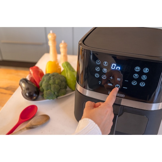 BLACKDECKER AFDLG air fryer touchscreen being operated in kitchen with vegetables and utensils nearby.
