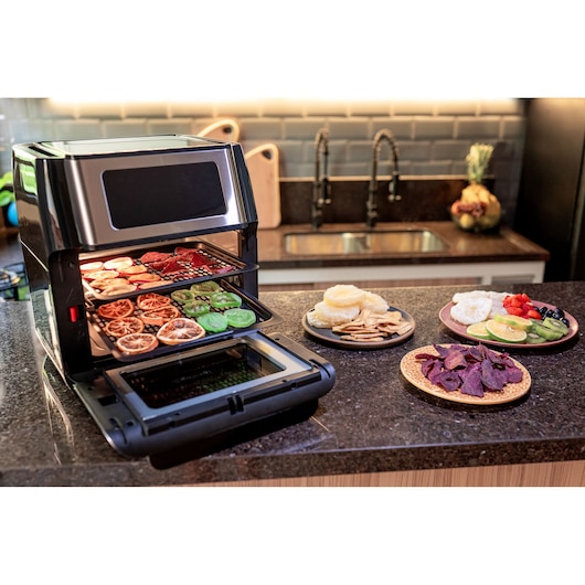 Photo of BLACKDECKER AFO12G countertop air fryer oven with trays of dried fruits, shown in a kitchen setting.