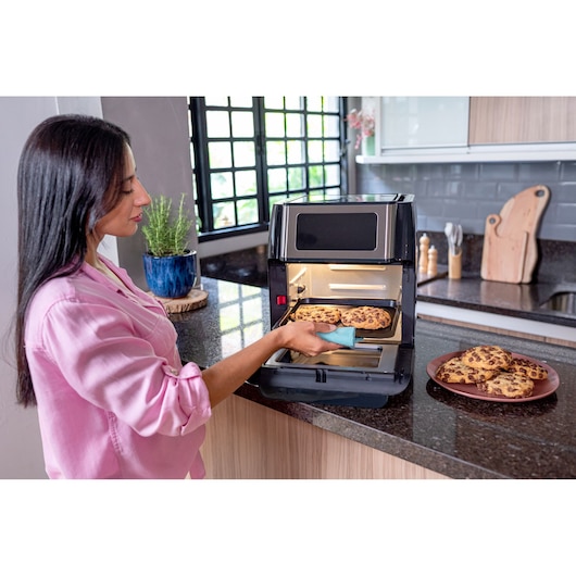 BLACKDECKER AFO12G countertop oven in use, person removing a tray of baked cookies in a modern kitchen.