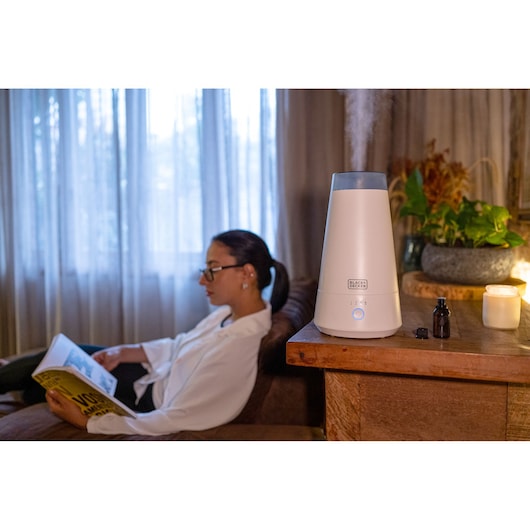 BLACK+DECKER AIR2000N air humidifier on wooden table, steam on, next to candle and oil bottle, cozy room background.