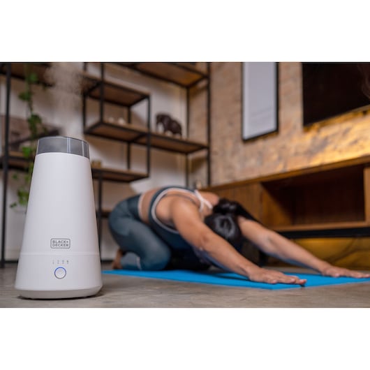 BLACKDECKER AIR2000N white humidifier on floor in front of person doing yoga indoors.