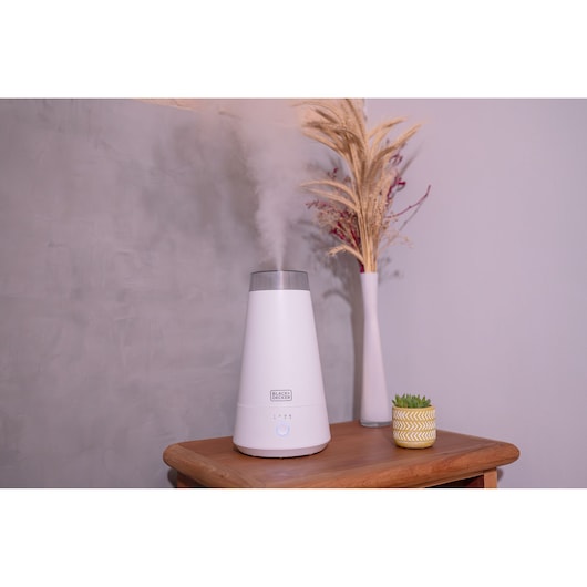 Photo of BLACKDECKER AIR2000N white humidifier on wooden table, mist output visible, vase and plant nearby.