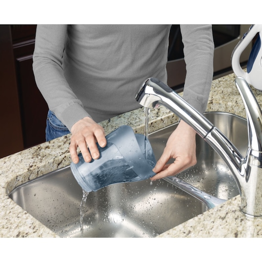 BLACKDECKER APB12000 dust container being rinsed under faucet in kitchen sink.