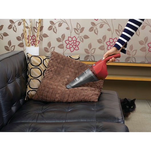 Photo of BLACK+DECKER APB3600 handheld vacuum cleaning a brown cushion on a black sofa in a living room.