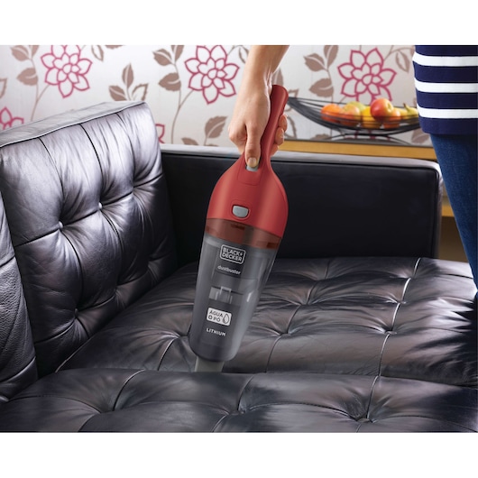 BLACKDECKER APB3600 handheld vacuum cleaner with red handle cleaning black leather sofa.