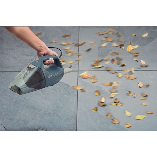 BLACKDECKER APS1200PET handheld vacuum blowing leaves on gray tile floor, pictured from above.