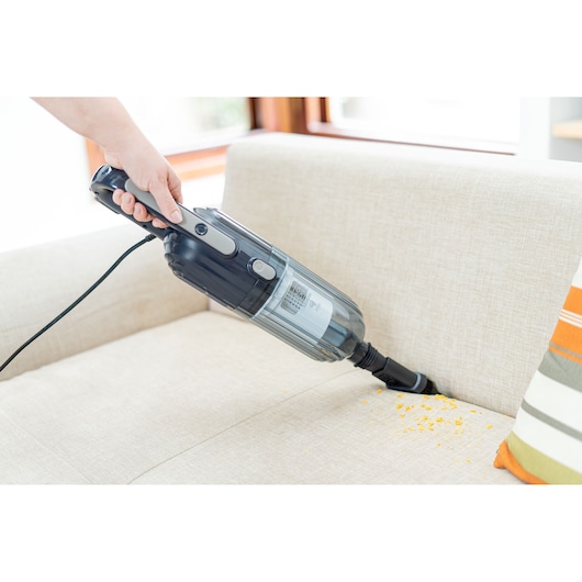BLACKDECKER AV15 handheld vacuum cleaner used to clean crumbs from a beige sofa.