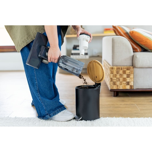 BLACKDECKER AV15 handheld vacuum dirt cup being emptied into a black trash can in a living room.