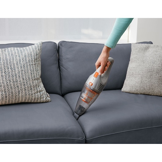 BLACKDECKER AV160 handheld vacuum cleaner being used to clean a dark gray sofa with decorative pillows.