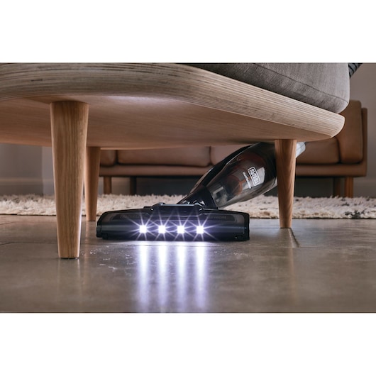 BLACK+DECKER AV160 cordless vacuum with LED lights cleaning under a sofa on a tile floor.