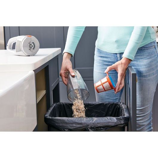 BLACKDECKER AV160 handheld vacuum being emptied into a trash bin in a kitchen, close-up side angle.