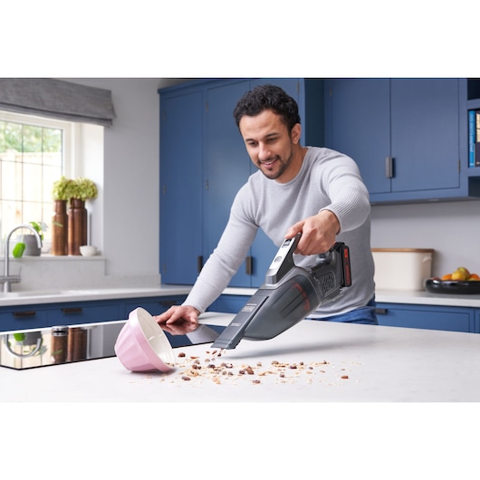 Photo of BLACKDECKER BCHV001D1E handheld vacuum cleaning crumbs from a kitchen counter near a pink bowl.