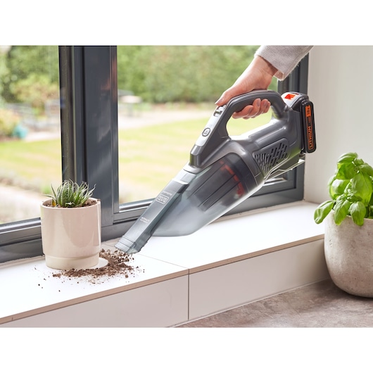Photo of BLACKDECKER BCHV001D1E handheld vacuum cleaning soil from windowsill near potted plants.