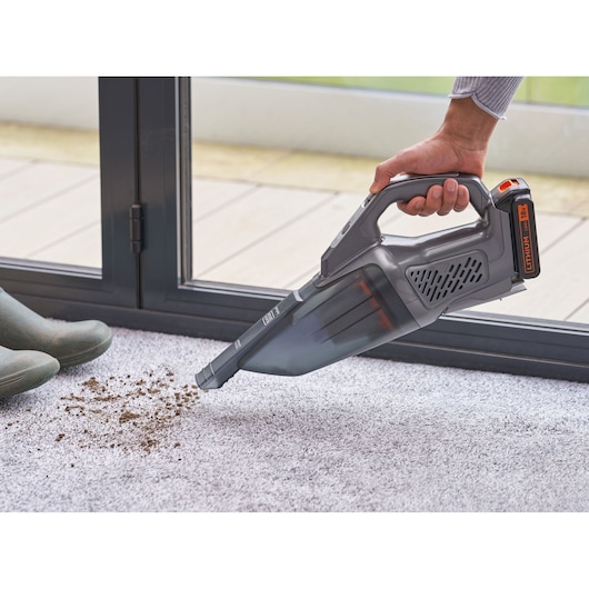 Photo of BLACKDECKER BCHV001D1E handheld vacuum cleaning dirt from carpet near boots indoors.