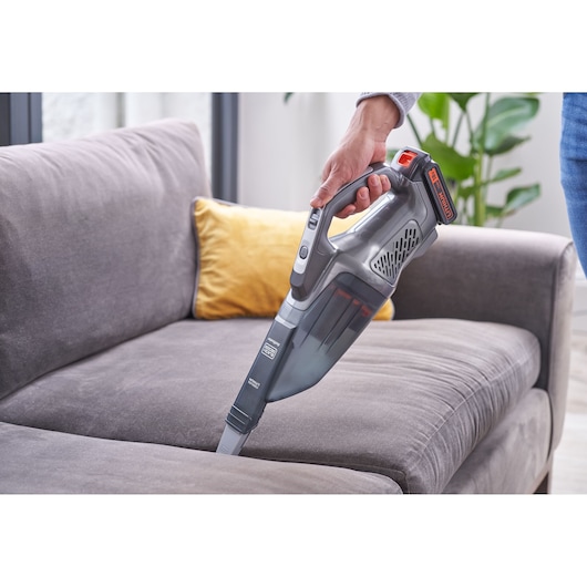 BLACKDECKER BCHV001D1E handheld vacuum cleaning a gray fabric sofa with a yellow pillow in a living room.