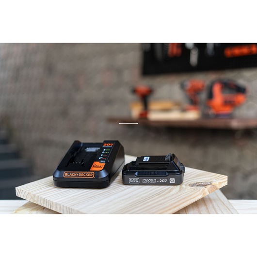 Photo of BLACK+DECKER BDL2020S 20V battery charger and lithium battery on a wooden board in a workshop setting.