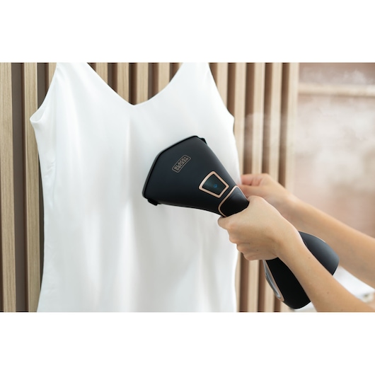 BLACKDECKER BDV2200 handheld steamer in use on a white garment, steaming out wrinkles, photography.