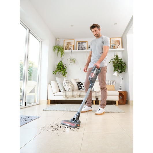 Photo of BLACKDECKER BHFEA18D1 cordless stick vacuum cleaning debris from tile floor in modern living room.