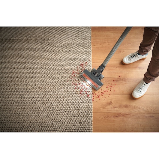 BLACKDECKER BHFEA18D1 cordless stick vacuum cleaning red debris from rug and hardwood floor, top-down view.
