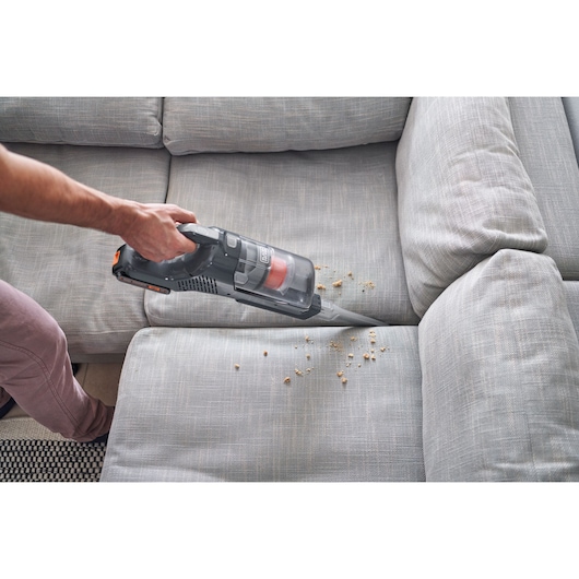 Photo of BLACK+DECKER BHFEA18D1 handheld vacuum cleaning crumbs from a light gray fabric sofa.