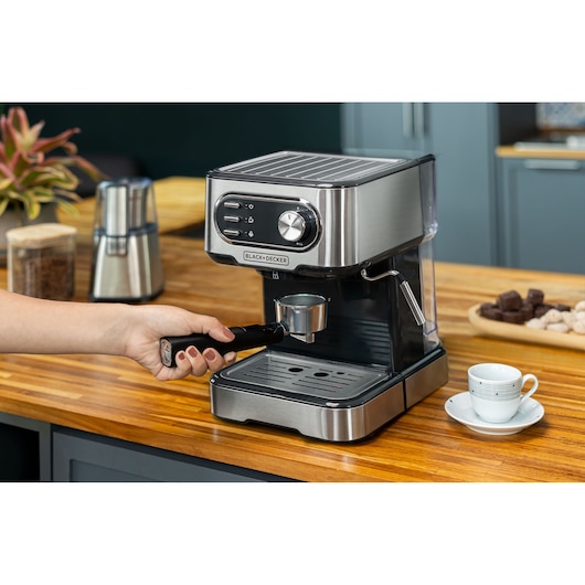 BLACKDECKER CE1100G espresso machine on wooden counter with a hand placing portafilter, cup nearby.