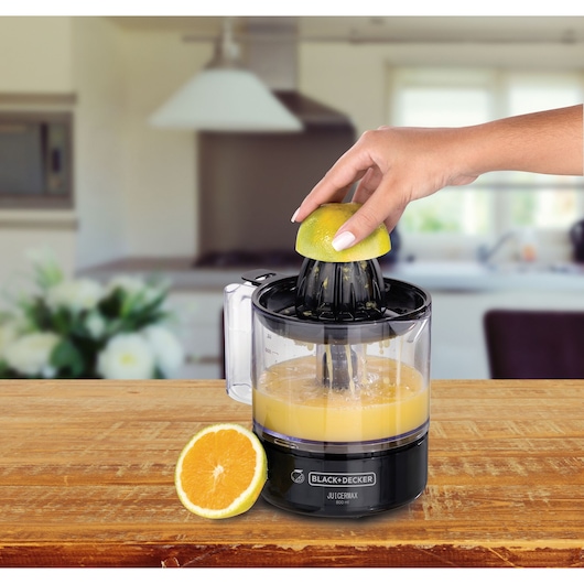 BLACK+DECKER CJ700 juicer on a kitchen counter squeezing orange juice, half orange in hand, sliced orange beside.
