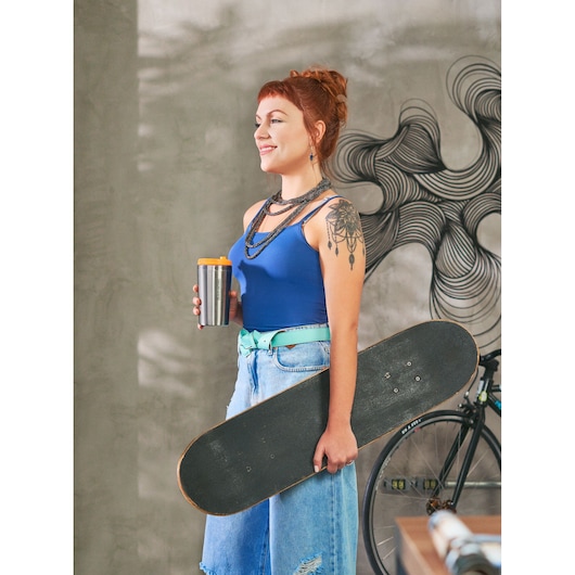 BLACKDECKER CM01 travel mug held by person in blue tank top and jeans with skateboard, indoor urban setting.