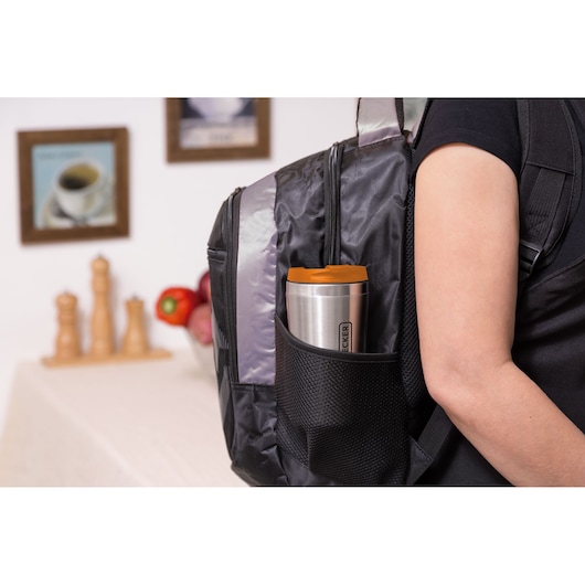 BLACKDECKER CM01 stainless steel travel mug with orange lid in backpack side pocket, indoor setting.