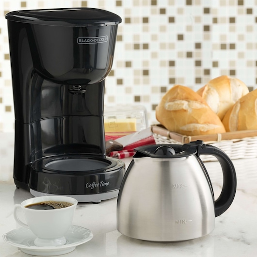 BLACK+DECKER CM15 black drip coffee maker with stainless steel carafe, cup of coffee, and bread on kitchen counter.
