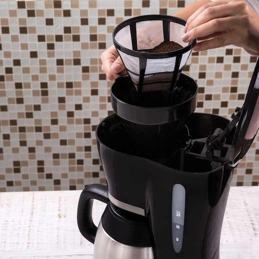 BLACKDECKER CM200I coffee maker on table, hand placing filter with ground coffee inside open lid.
