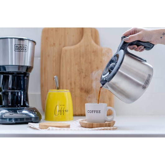 BLACKDECKER CM250P coffee maker with stainless steel carafe pouring hot coffee into mug in kitchen setting
