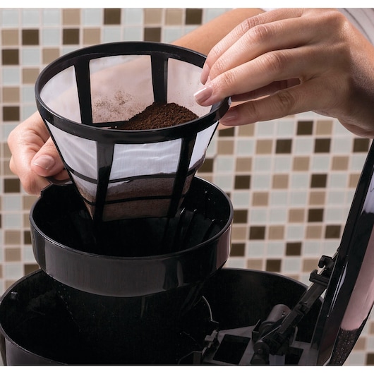 BLACKDECKER CM38 coffee maker filter filled with ground coffee being placed in black coffee machine, close-up.