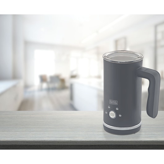BLACK+DECKER electric milk frother model EL500 in dark gray color placed on a kitchen countertop with a blurred modern kitchen in the background.