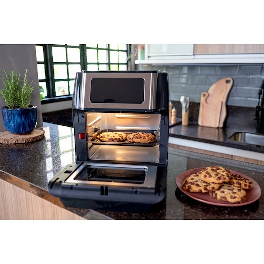 oven with the lid open, under a counter, showing ready-made cookies. Cookies inside and outside the tray.