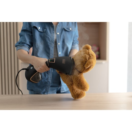 Hand holding Garment Steamershowing digital painel in use for Teddy bear