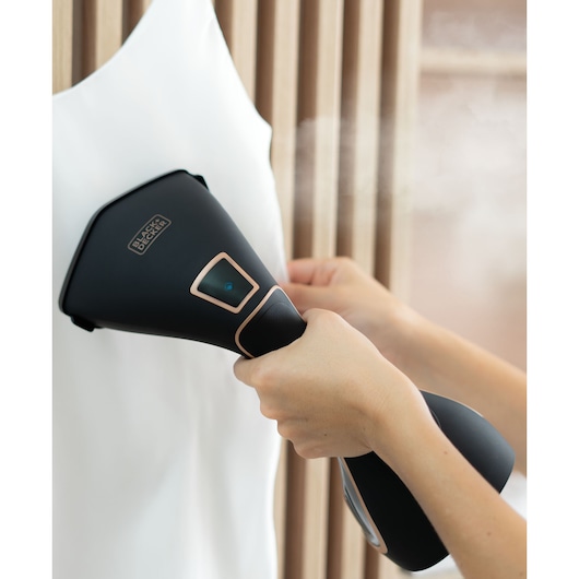 Hand holding Garment Steamer showing digital painel in use in white t-shirt
