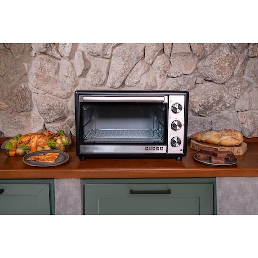 FT46 family size oven on a countertop. On one side of the oven roast chicken, a piece of pizza and on the other side brownie and bread.