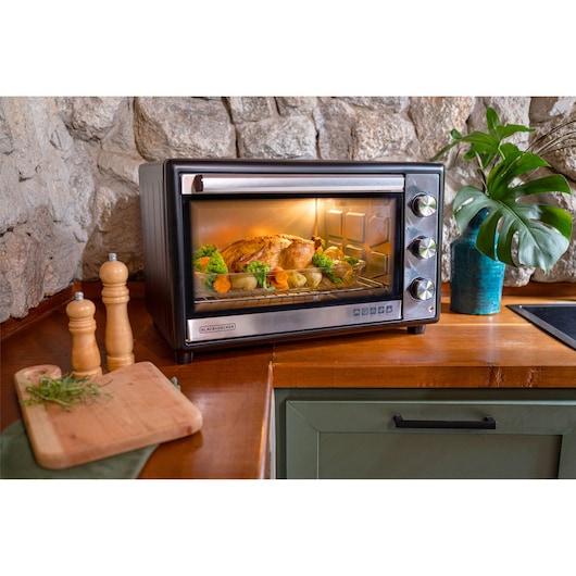 FT46 family size oven on a countertop. On one side of the oven roast chicken, a piece of pizza and on the other side brownie and bread.