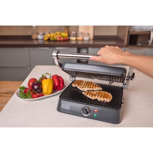 grill G1400 BLACK and Decker. Open under the table with 2 chicken fillet under the grill. A hand holding the half open grill handle.