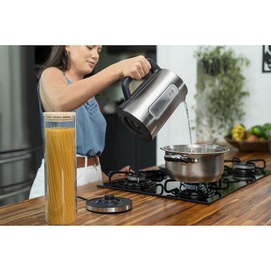 Programmable Electric Kettle. A woman uses a kettle to put water in a pan on the stove. She will prepare pasta, the food is next to the stove.