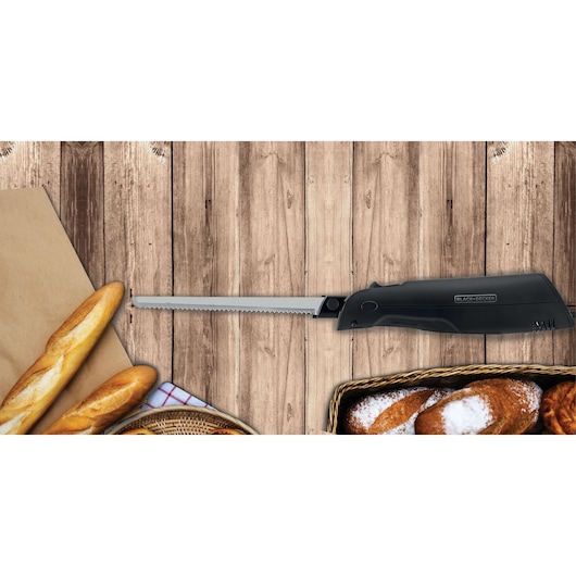 Photo of BLACK+DECKER electric knife FEL150 on wood background with assorted bread, left side view.
