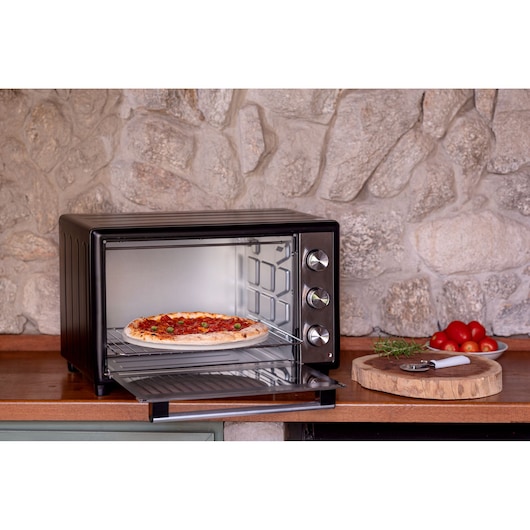 BLACKDECKER FT46 countertop oven with pizza on rack, three control knobs, kitchen scene with tomatoes and herbs.