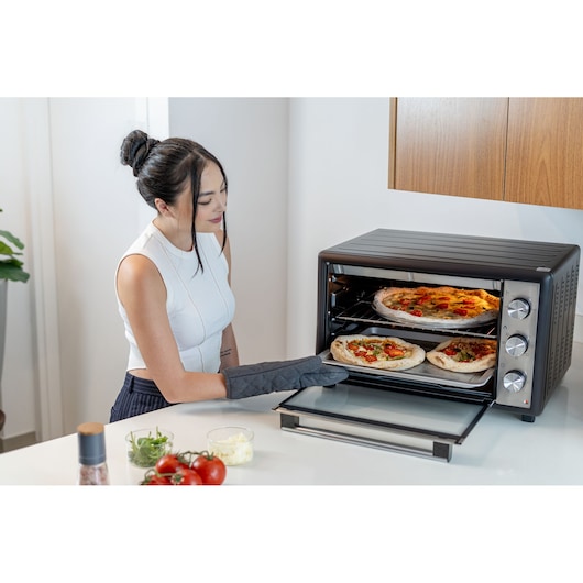 Photo of person using BLACKDECKER FT60 countertop oven to bake pizzas in a modern kitchen.