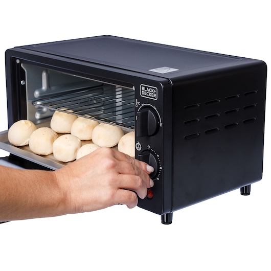Photo of BLACK+DECKER FT9N toaster oven with hand turning dial, tray of dough balls inside, white background.
