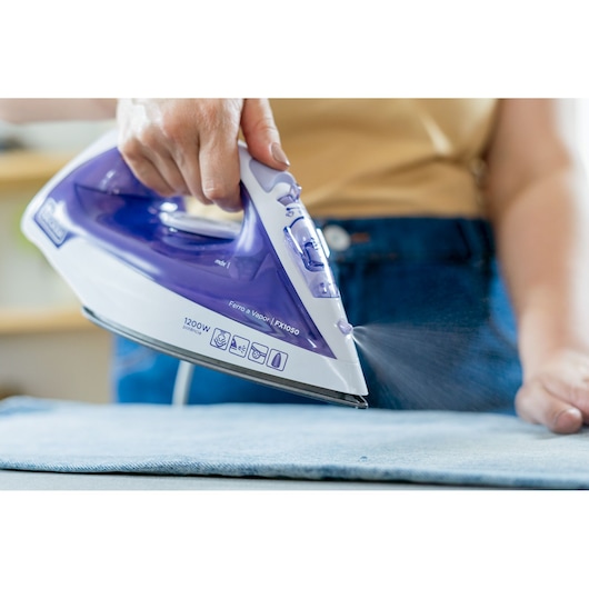 BLACKDECKER FX1050 purple and white steam iron in use on fabric, close-up side angle.
