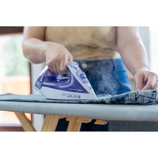 BLACKDECKER FX1050 steam iron with purple and white design ironing denim on ironing board.