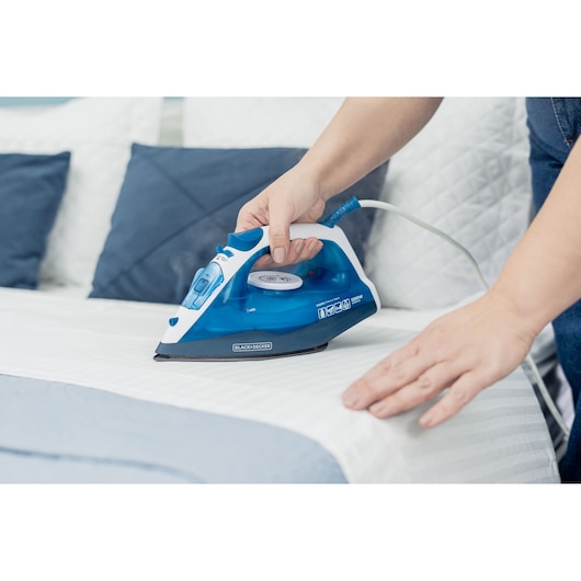 BLACK+DECKER FX2150 steam iron with blue and white body used on striped bedding.